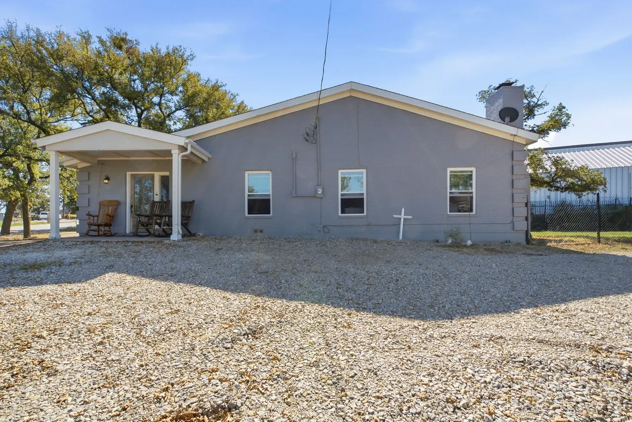 Straight-on view of the house front with its covered porch and gravel yard