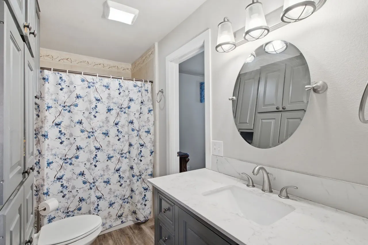 Hall bathroom with a tub and shower curtain, a vanity and round mirror