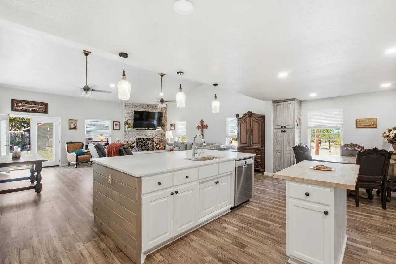 White kitchen with a quartz island and pendant lights, open to the living room and fireplace