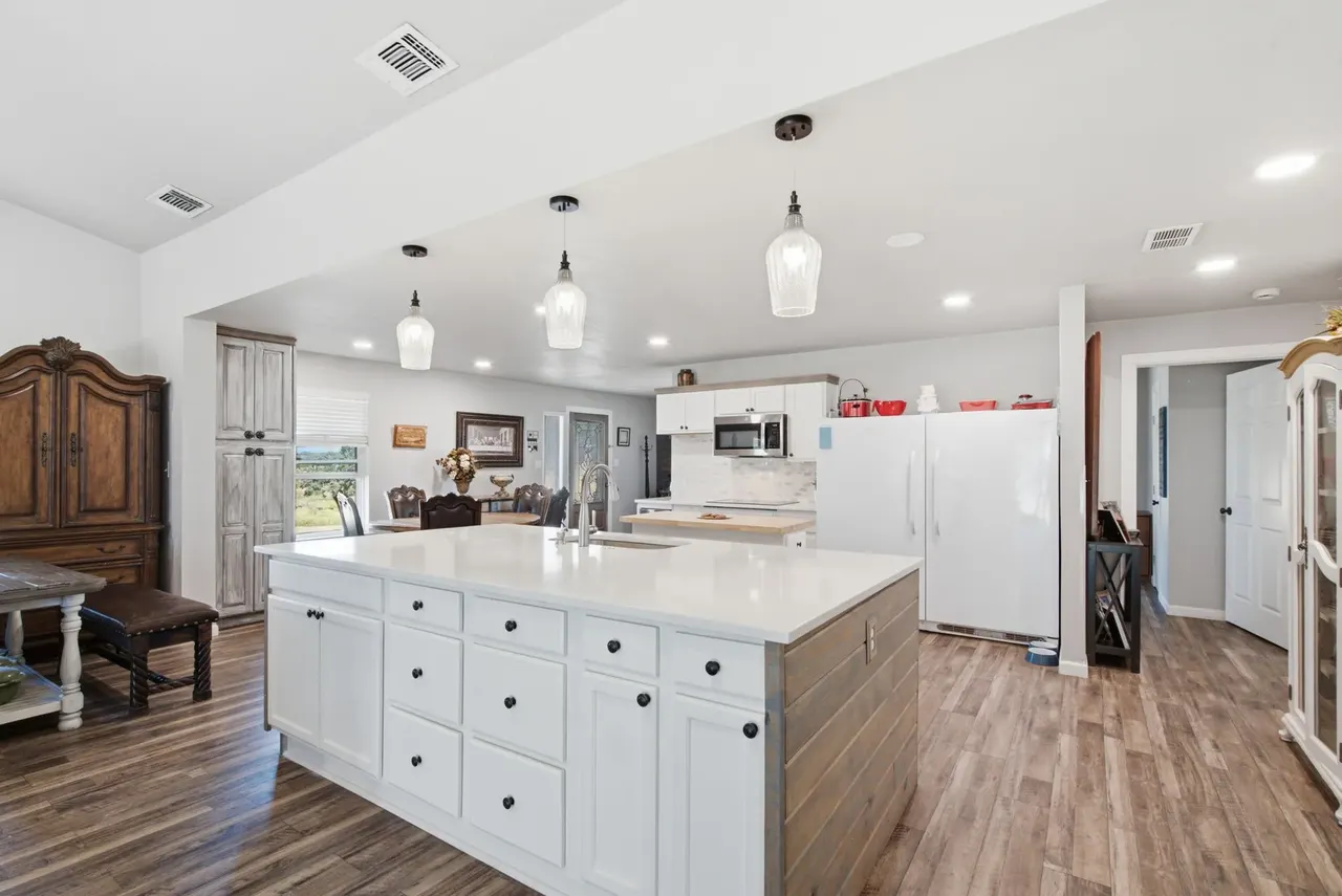 Kitchen with a long white quartz island, pendant lights and an armoire