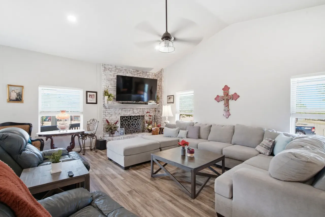 Living room with a vaulted ceiling, whitewashed brick fireplace and a large gray sectional