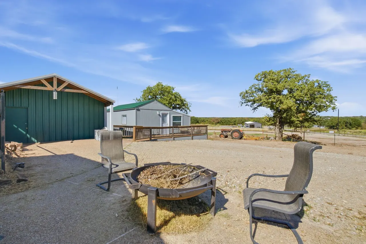 Fire pit with patio chairs on gravel, the green shop behind